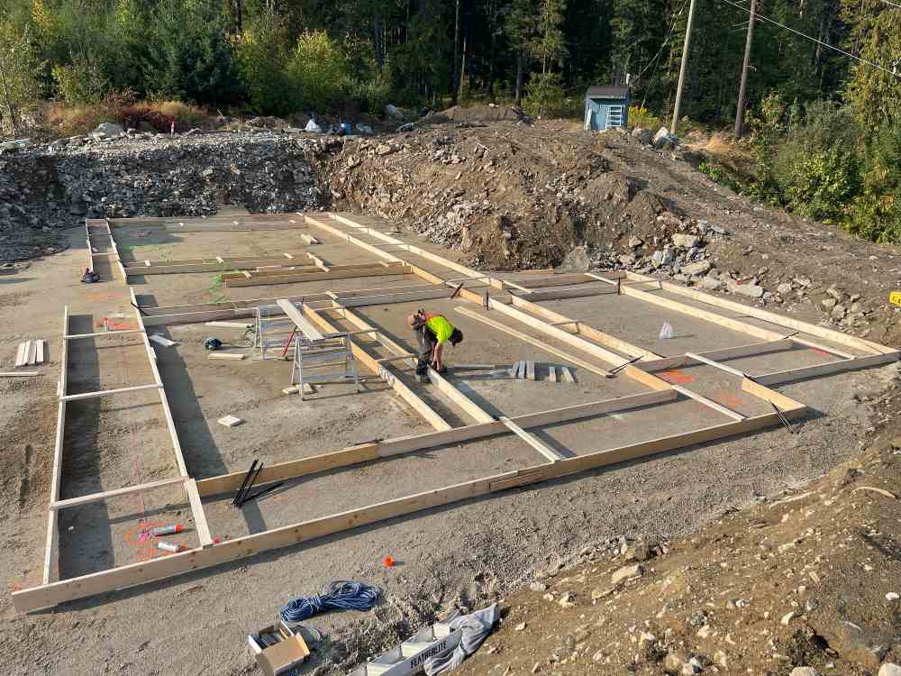 A construction worker laying out wood planks on an empty lot for site preparation purposes.